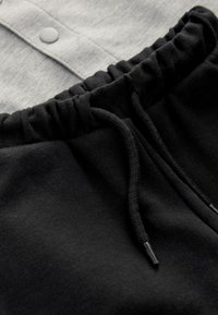 Chemise grise à boutons avec une ceinture élastique noire et un cordon de serrage. Tissu en mélange de coton lisse et lignes simples et épurées.