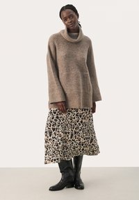 Beige Strickpullover mit Schalkragen; kombiniert mit einem Midirock im Leopardenmuster; das Model trägt kniehohe schwarze Stiefel; weiche Texturen und fließendes Design.