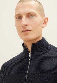 Marineblauer, gerippter Reißverschluss-Pullover mit hohem Kragen. Verfügt über einen silbernen Reißverschluss und strukturierte Details über der Brust und an den Schultern.