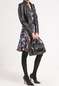 Veste en cuir noir sur une robe fleurie, collants noirs et escarpins noirs. Portant un sac à main noir avec un détail en franges.