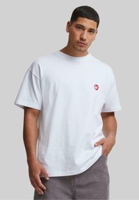 Hvid bomulds t-shirt med et lille rødt hjerte logo på venstre bryst, afslappet pasform, korte ærmer og en glat tekstur.