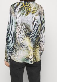 Sileä, monivärinen pusero, jossa on kirkas eläinkuosi vihreillä, keltaisilla, mustilla ja beigen sävyisillä kuvioilla. Pitkät hihat, joissa nappikiinnitteiset kalvosimet.