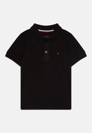 Fekete, rövid ujjú polo ing, két gombbal, kis hímzett logóval a mellkason, valamint piros és fehér belső díszítésű gallérral.