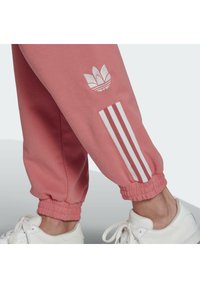 Onderbenen met roze joggingbroeken met wit Adidas-logo en drie strepen boven de elastische boorden, gecombineerd met witte sneakers.