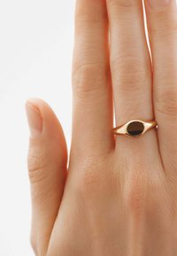 Anillo de oro con piedra ovalada negra, con una superficie lisa y forma redondeada, llevado en una mano contra un fondo claro.