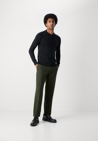 Polo noir à manches longues avec patte de boutonnage, associé à un pantalon vert olive et des chaussures noires à lacets. Tissu lisse avec une coupe ajustée.