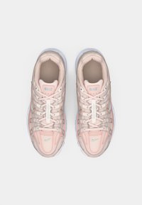 Gaiši rozā Nike skriešanas kurpes ar pelēkiem akcentiem, sieta audums un auklas, skatīts no augšas uz vienkārša balta fona.