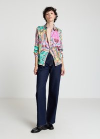 Chemise à motifs colorés dans des tons vifs de rose, vert et jaune avec des détails floraux, associée à un pantalon en denim foncé taille haute et des chaussures noires.