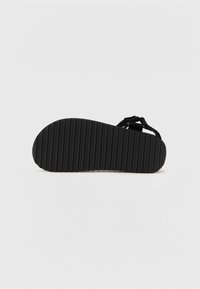 Sandale noire avec une semelle texturée et striée ainsi que des lanières réglables. Le design simple met l'accent sur la fonctionnalité et le confort.