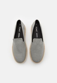 Chaussures grises sans lacets en tissu texturé avec un bout arrondi et une semelle de style jute. L'intérieur comprend un rembourrage noir avec l'étiquette de la marque.