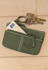 Zelená kožená klíčenka s bílým prošitím, částečně rozzipovaná, uvnitř složená eurobankovka, připojená ke třem kovovým klíčům na kroužku.