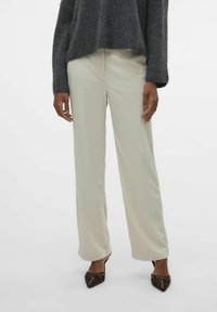 Lichte beige, wijde broek met een geribbelde textuur, gecombineerd met een donkergrijze oversized trui en puntige bruine hakken.