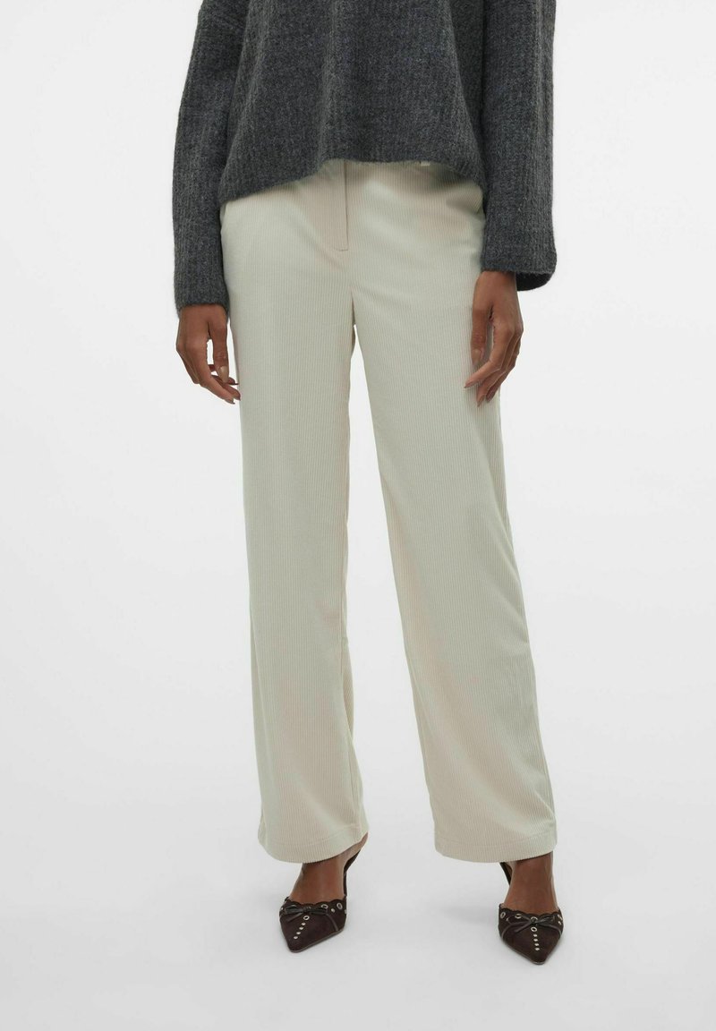 Lichte beige, wijde broek met een geribbelde textuur, gecombineerd met een donkergrijze oversized trui en puntige bruine hakken.