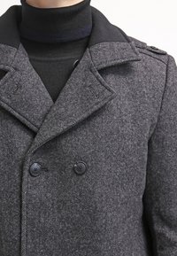 Cappotto grigio in misto lana con chiusura doppiopetto, bottoni grandi e colletto strutturato, realizzato in un tessuto texturizzato e dotato di epaulettes sulle spalle.