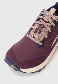 Ljubičaste trkačke tenisice s teksturiranim gornjim dijelom, kremastom potplatom i kontrastnim plavim akcentima. vezice imaju tkanu uzorak; logo Vibram je vidljiv.