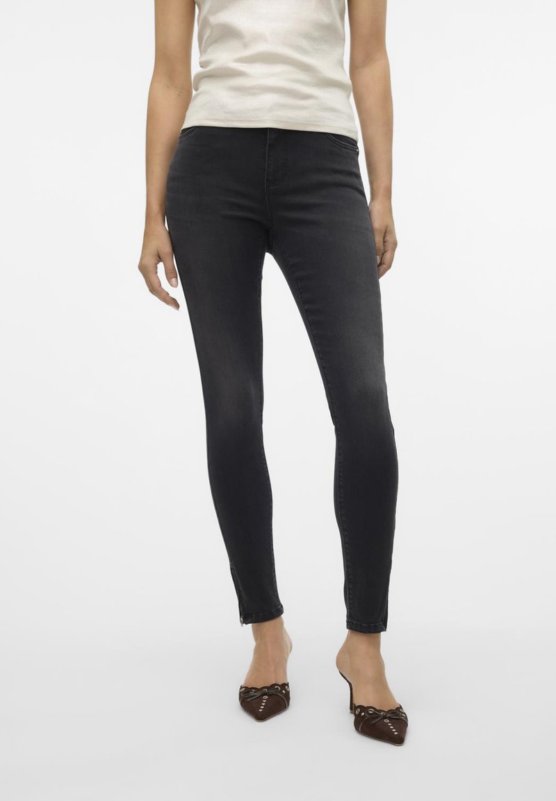 Zwarte slim-fit jeans met een gladde textuur, uitgerust met een middelhoge taille en een klassiek vijf-pocketdesign. Gecombineerd met een lichtgekleurde top en bruine schoenen.