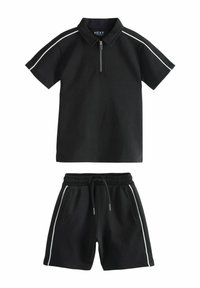 Fekete póló, cipzáros gallérral és fehér oldalsávokkal, párosítva fekete rövidnadrággal, amely rugalmas derékkal és oldalsó zsebekkel rendelkezik.