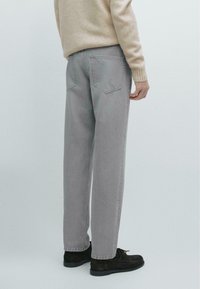 Gray denim trousers with a relaxed fit, featuring back pockets and a stitched waistband, paired with dark shoes. Soft, textured fabric.