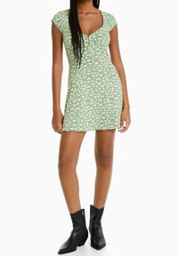 Vihreä, kukkakuosinen mekko, jossa on lyhyet hihattomat hihat, pyöreä pääntie ja istuva muoto, yhdistettynä mustiin nilkkasaappaisiin.