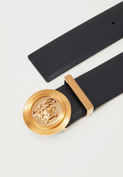 Must mustriba mustridast kuldne medaljon, millel on väljakasvatatud nägu motiiv. Tekstureeritud kuldsed aktsendid rõhutavad disaini.