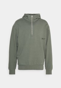 Sudadera verde con cuello alto tipo embudo y cremallera de media longitud. Presenta puños acanalados y un pequeño logotipo negro en el pecho. Textura suave.