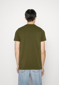 Camiseta de manga corta en verde oliva con cuello redondo. Fabricada en algodón suave, presenta un corte recto y un pequeño detalle del logo cerca del dobladillo.