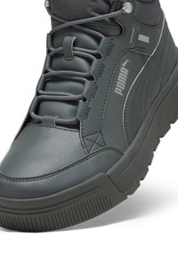 Gros plan sur une basket montante Puma gris foncé en cuir texturé, avec des lacets et une semelle épaisse.