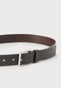 Καφέ δερμάτινη ζώνη με ασημένια μεταλλική αγκράφα. Διαθέτει πολλαπλές τρύπες για ρύθμιση μεγέθους και ομαλή, στιλβωμένη υφή.