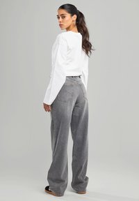 Top blanco de manga larga y ligera combinado con pantalones de mezclilla grises de tiro alto y corte holgado. Con bolsillos notables y detalles de costura sutiles.