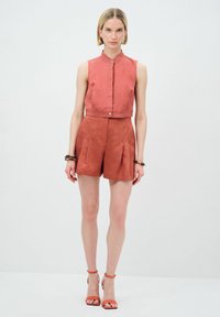 Rotes Leinen-Cropped-Top ohne Ärmel mit einem Mandarin-Kragen, kombiniert mit passenden hoch taillierten Shorts mit Falten und Seitentaschen.
