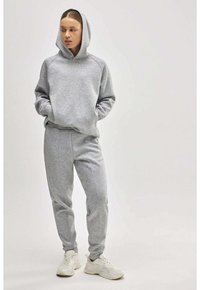 Sudadera gris con capucha y pantalones jogger a juego. Tejido suave y texturizado con puños y costuras laterales acanaladas. Zapatillas blancas completan el conjunto.