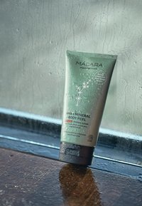 Grön tub av Mádara AHA + Mineral Body Peel. Har en matt finish, silvertext och en svart bas. Synliga vattendroppar på ytan.