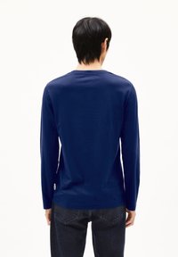 Marineblaues Langarmshirt aus weichem Baumwollmaterial, mit Rundhalsausschnitt und geradem Schnitt, kombiniert mit dunklen Jeans. Minimale Markenkennzeichnung sichtbar.