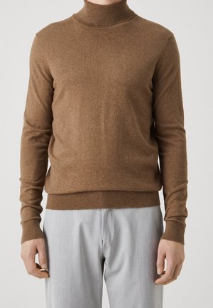 Brauner Rollkragenpullover aus weichem Strickstoff, mit langen Ärmeln und tailliertem Schnitt, kombiniert mit hellgrauen Hosen.