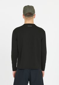 Schwarzes Langarmshirt mit Rundhalsausschnitt, aus weicher Baumwolle, mit einem dezenten Logo auf dem Rücken und vor einem schlichten Hintergrund.