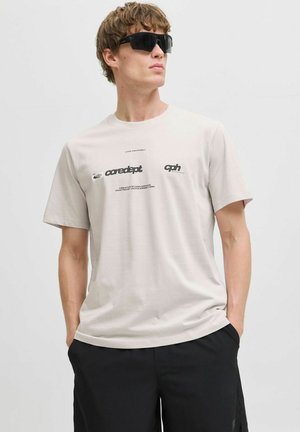 Light beige cotton T-shirt with black text graphics; round neckline, short sleeves, paired with black shorts and dark sunglasses.