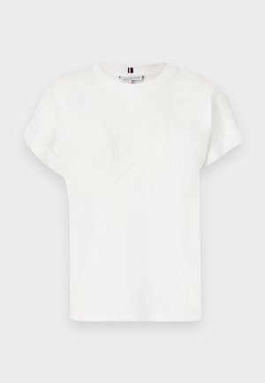 T-shirt blanc à manches courtes en coton, avec un logo en relief discret sur le devant et des poignets roulés. Texture lisse, coupe décontractée.