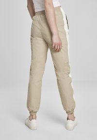 Lys beige joggebukser med elastiske ermer og elastisk midje, med sidestriper i hvitt og neongrønt. Glatt, lett materiale.