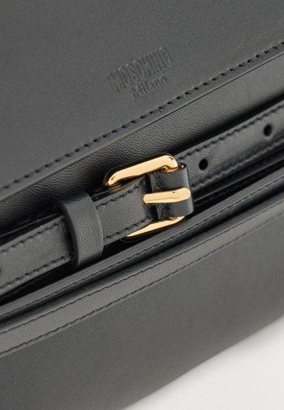 Μαύρη δερμάτινη τσάντα με αγκράφα σε χρυσή απόχρωση και ανάγλυφο λογότυπο "MOSCHINO Milano" πάνω από τον ιμάντα.
