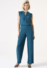 Turquoise tweed twee-delige jumpsuit met een top met gerimpelde aangeknipte mouwen en wijde pijpen, voorzien van een strikdetail bij de halslijn en een textuurstof.