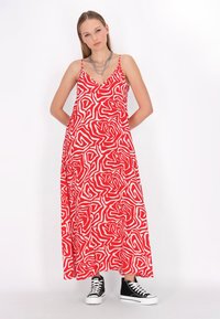 Rochie maxi roșie cu model abstract alb în spirală, decolteu în V, bretele subțiri și buzunare laterale; asortată cu teniși negri cu talpă înaltă.