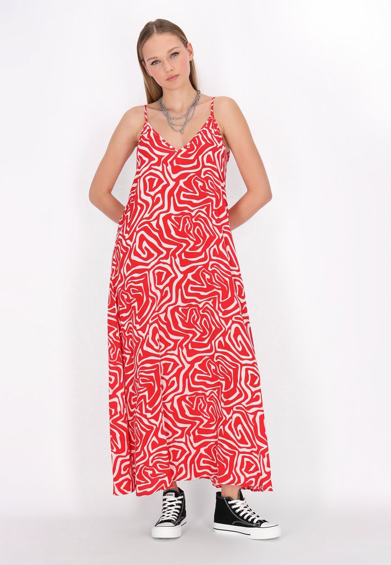 Rochie maxi roșie cu model abstract alb în spirală, decolteu în V, bretele subțiri și buzunare laterale; asortată cu teniși negri cu talpă înaltă.
