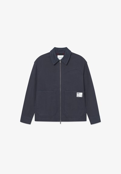 Chaqueta azul marino con cremallera frontal, bolsillos con parche y una pequeña etiqueta en el bolsillo izquierdo, con un cuello texturizado y una tela lisa.