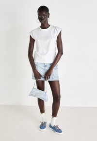 T-shirt branca de algodão com mangas enroladas, saia de ganga azul clara, ténis azuis com atacadores laranja, meias brancas até ao joelho e uma mala de designer.