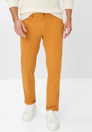 Herren-Hosen aus orangefarbener Baumwolle im Slim-Fit-Stil mit einem Knopfverschluss, Taschen vorne und hochgekrempelten Säumen, kombiniert mit weißen Sneakers.