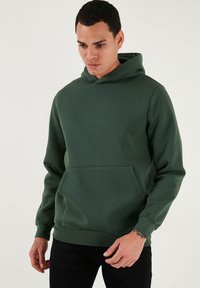 Zelená mikina s kapucňou, predným vreckom, dlhými rukávmi a rebrovanými manžetami. Vyrobená z hladkej, štruktúrovanej tkaniny.