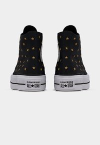 Μαύρα Converse All Star πάνινα παπούτσια ψηλά με χρυσό μοτίβο αστεριών, απεικονίζονται από πίσω σε λευκό φόντο.