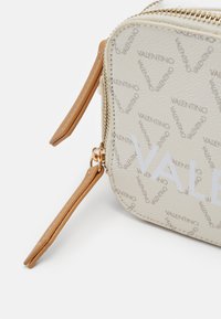 Bežinė odinė kišeninė rankinė su iškilniu "Valentino" logotipo raštu, auksinių detalizuotų elementų ir rudų odinių kutų. Kompaktiška stačiakampio formos.
