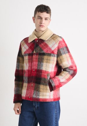 Plaid wool jacket in red, beige, and black. Features a cream-colored shearling collar, snap buttons, and side pockets. Textured finish.
