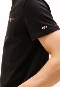 Czarny bawełniany t-shirt z krótkimi rękawami, z czerwoną i białą logotypem "Tommy Jeans" na klatce piersiowej oraz haftowanym logo na rękawie.